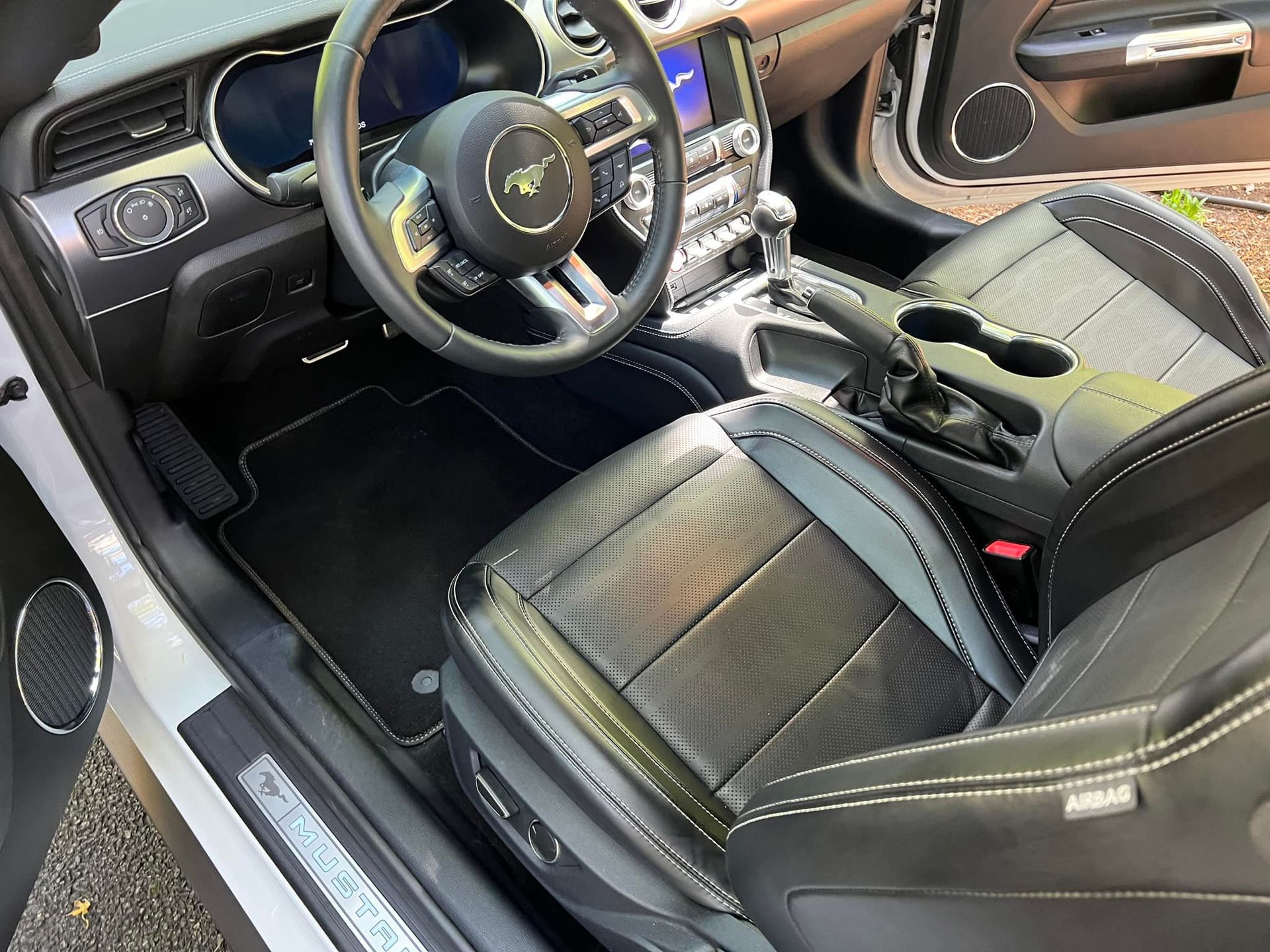 Black sports car interior with steering wheel, carbon-fiber trim, and leather seats, driver door open