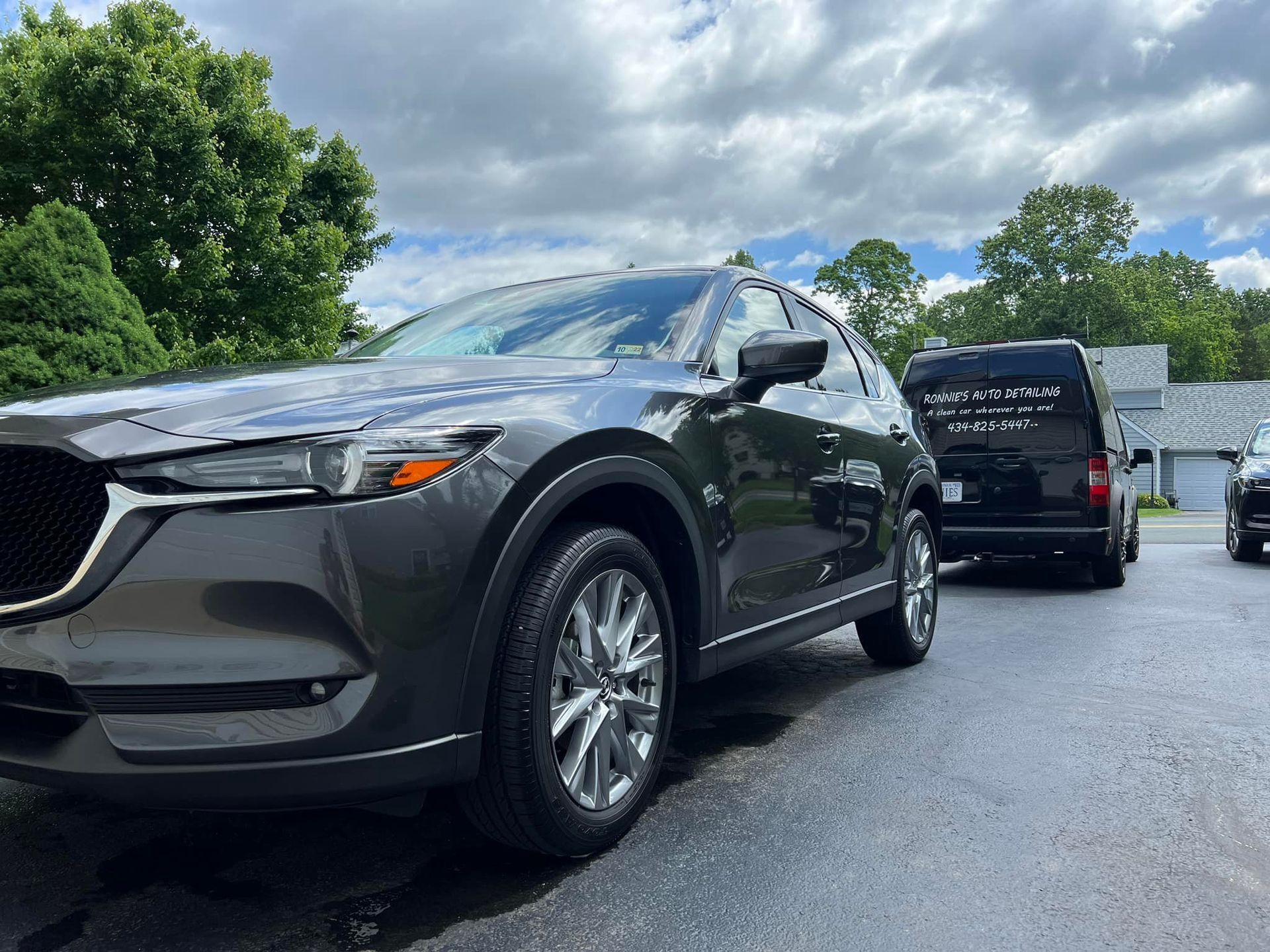 Dark gray SUV parked on a wet driveway beside a black van under cloudy skies