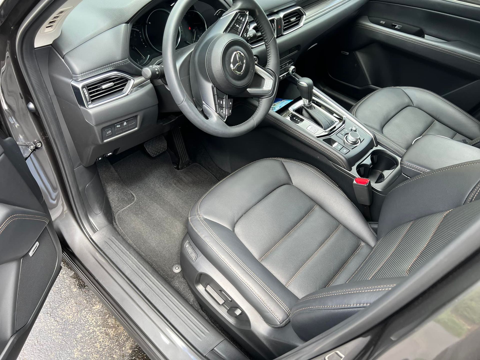 Car interior with black leather seats, steering wheel, and center console, viewed from the open driver’s door