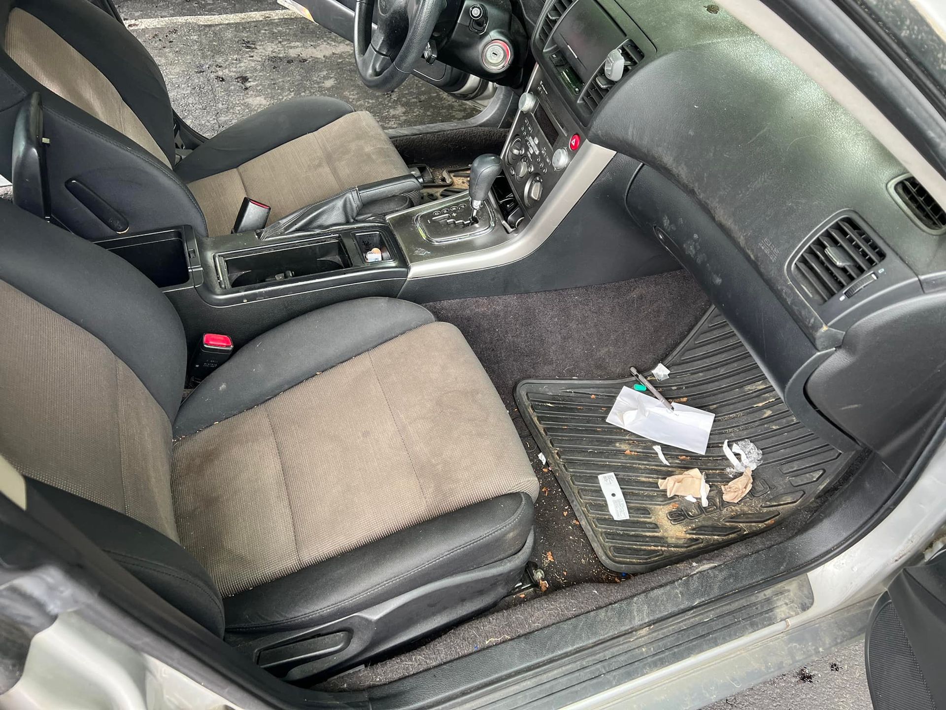 Car interior with black and gray seats and scattered trash on the passenger-side floor.