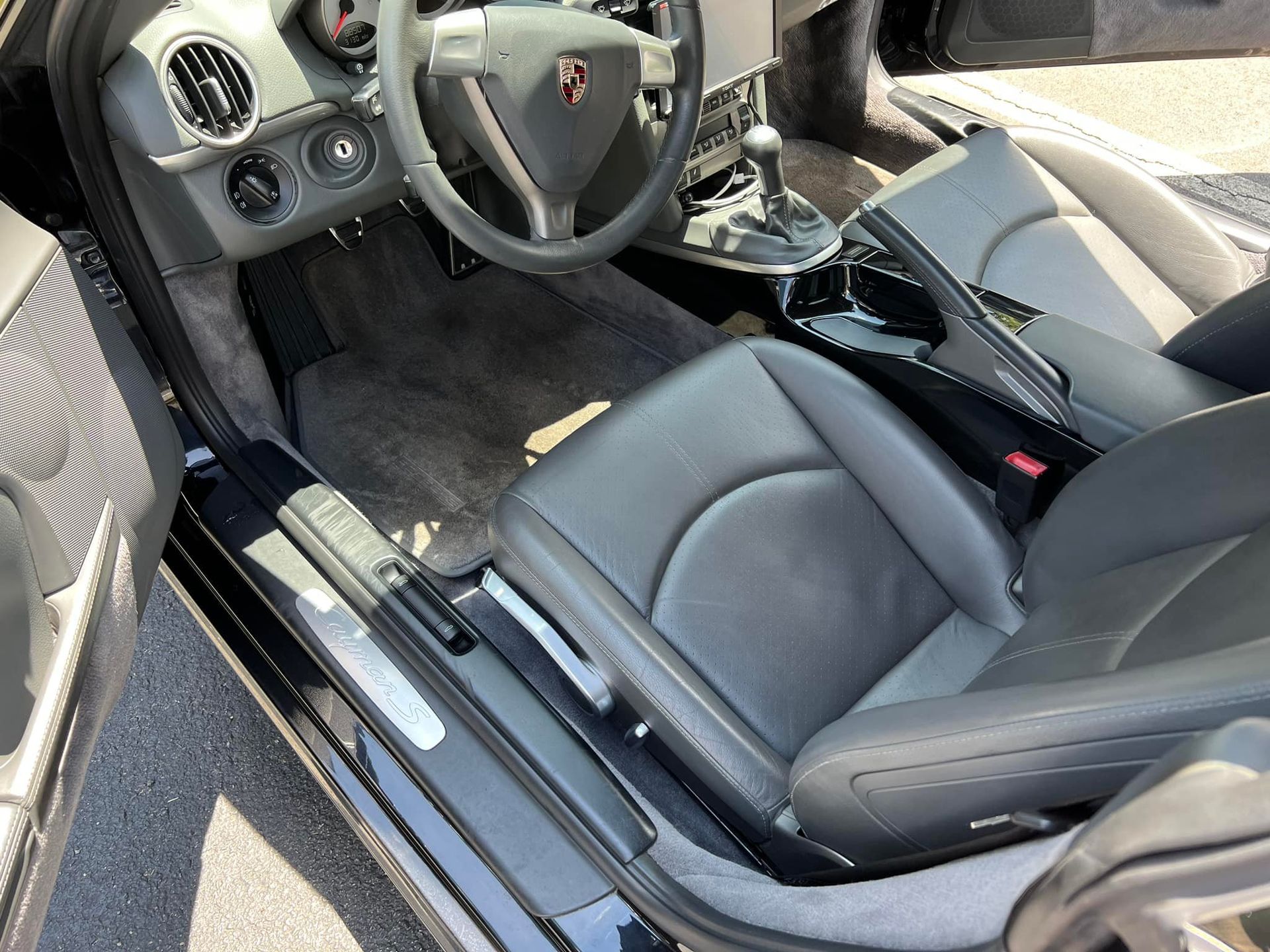 Car interior with black leather seats, center console, and steering wheel, viewed from the open driver’s door