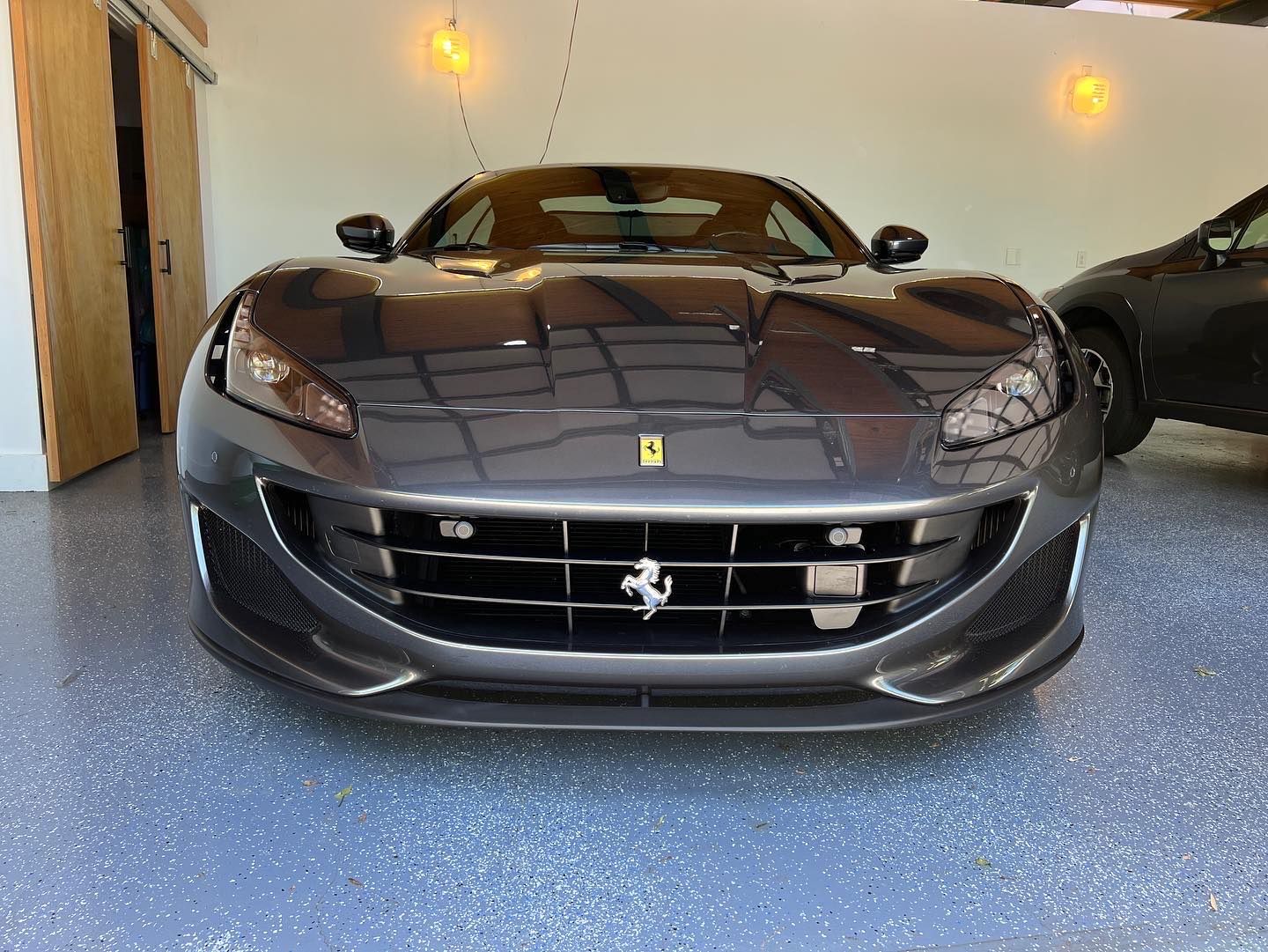 Black Ferrari sports car parked in a garage, front view.