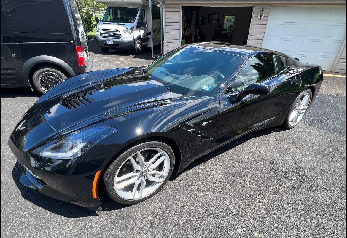 Black sports car parked in a driveway beside a garage, viewed from the front-left side.