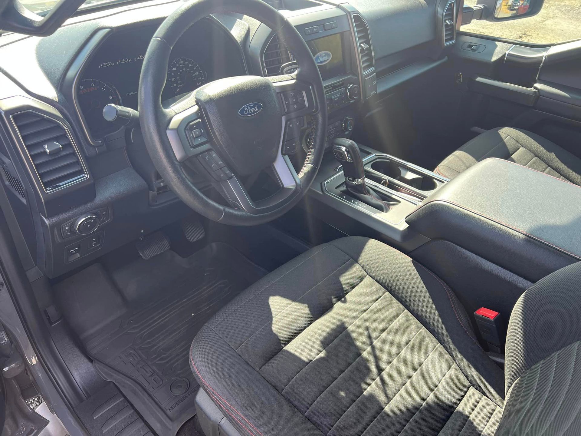 Car interior with black seats, steering wheel, center console, and sunlight streaming through the open door
