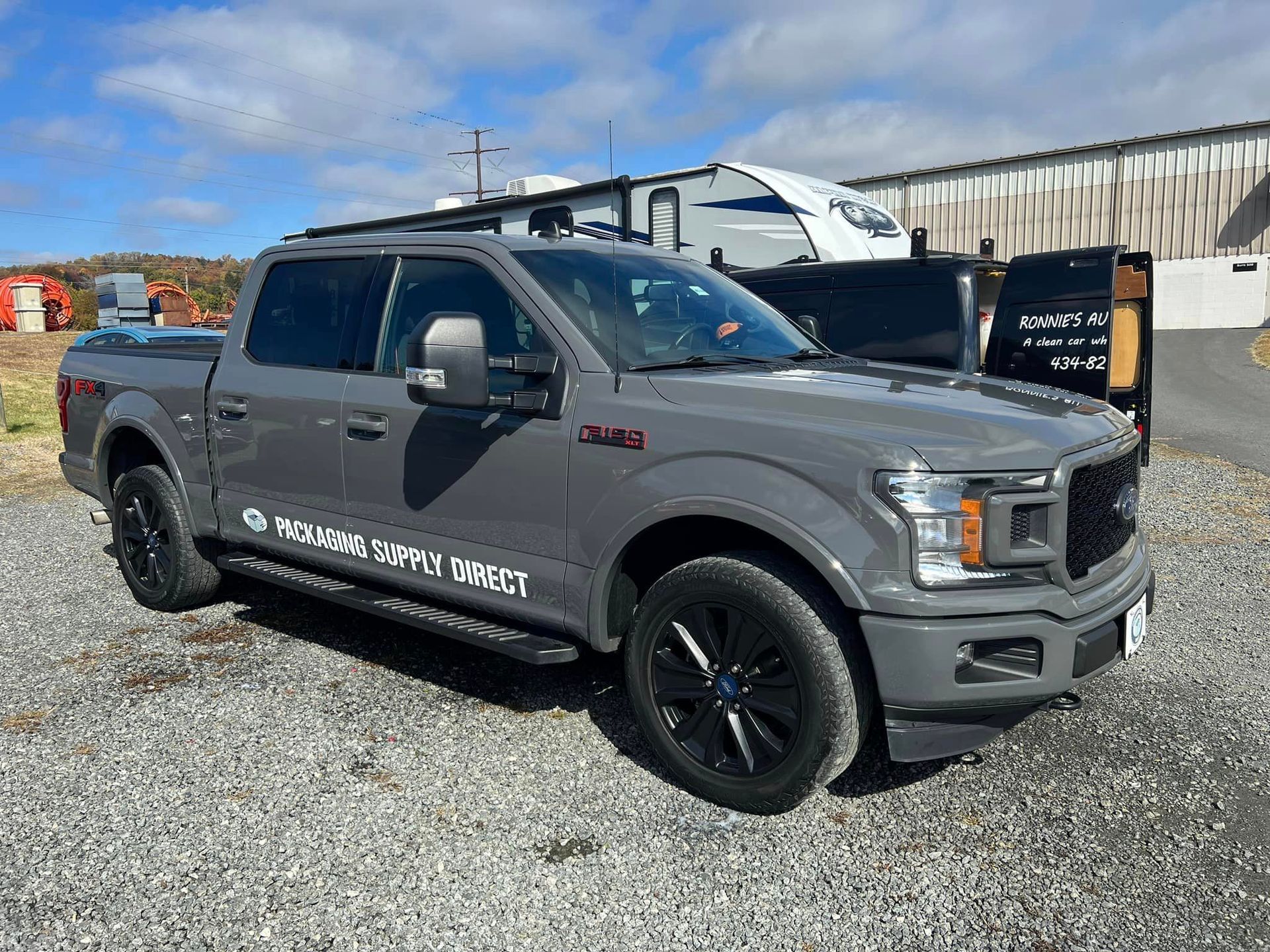 Gray pickup truck parked on gravel beside boats and a warehouse