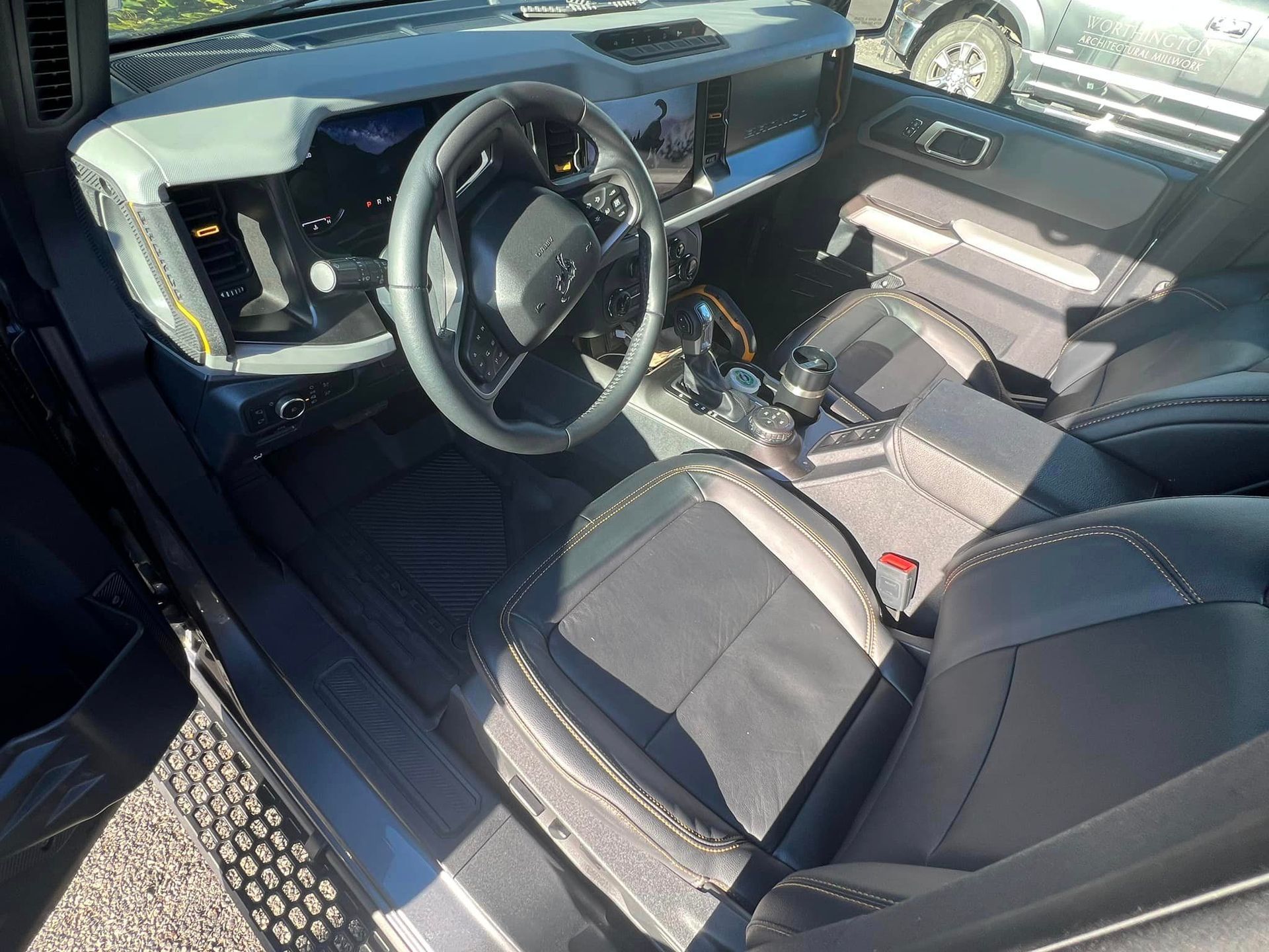 Black car interior with steering wheel, center console, and front seats in daylight