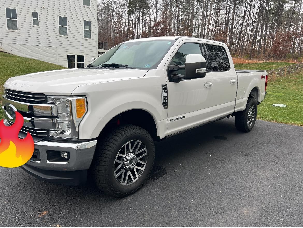 White pickup truck parked on a driveway beside a house, with a flame sticker on the front bumper