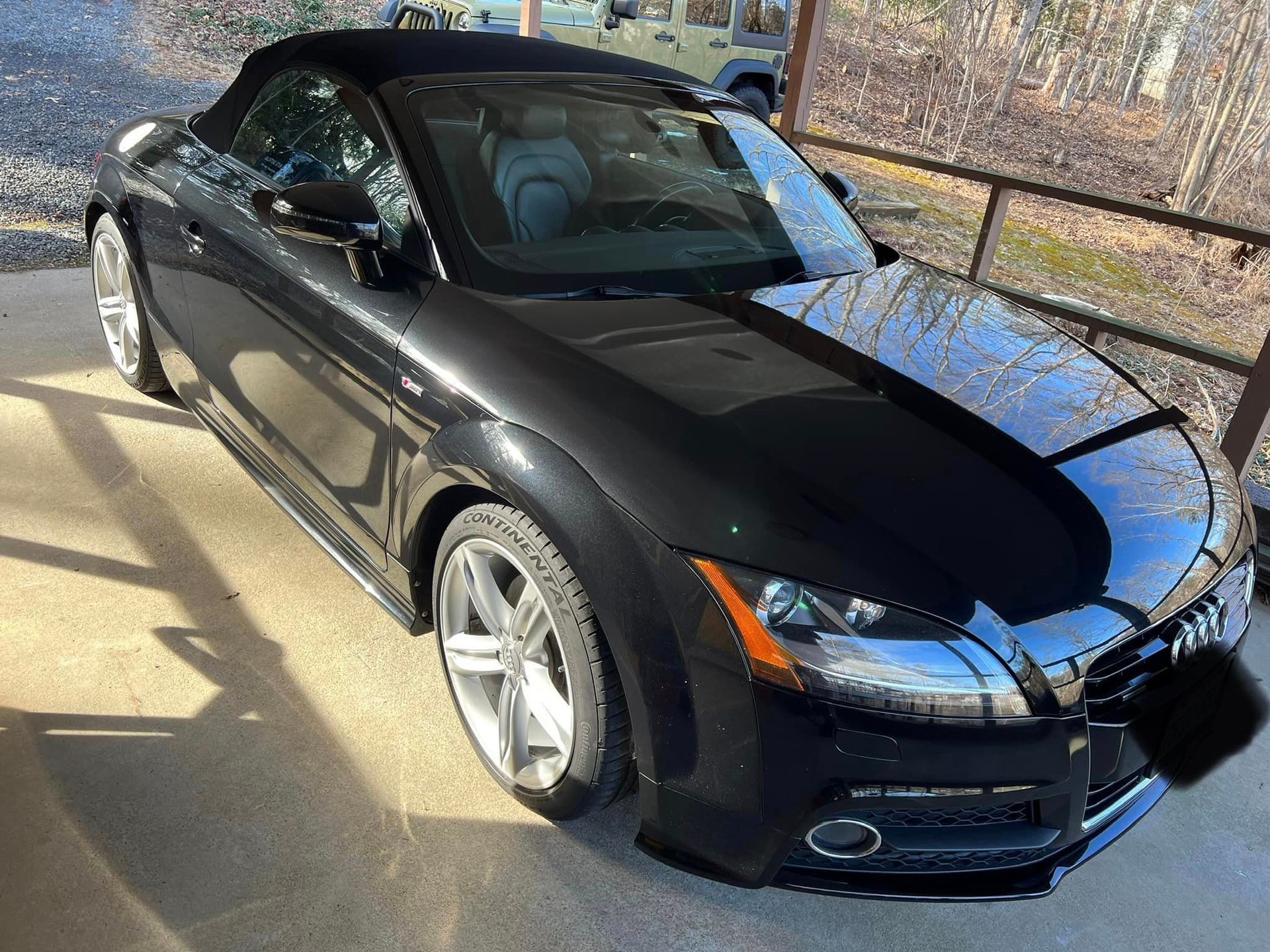 Black sports convertible parked outdoors in sunlight, viewed from the front-left side.
