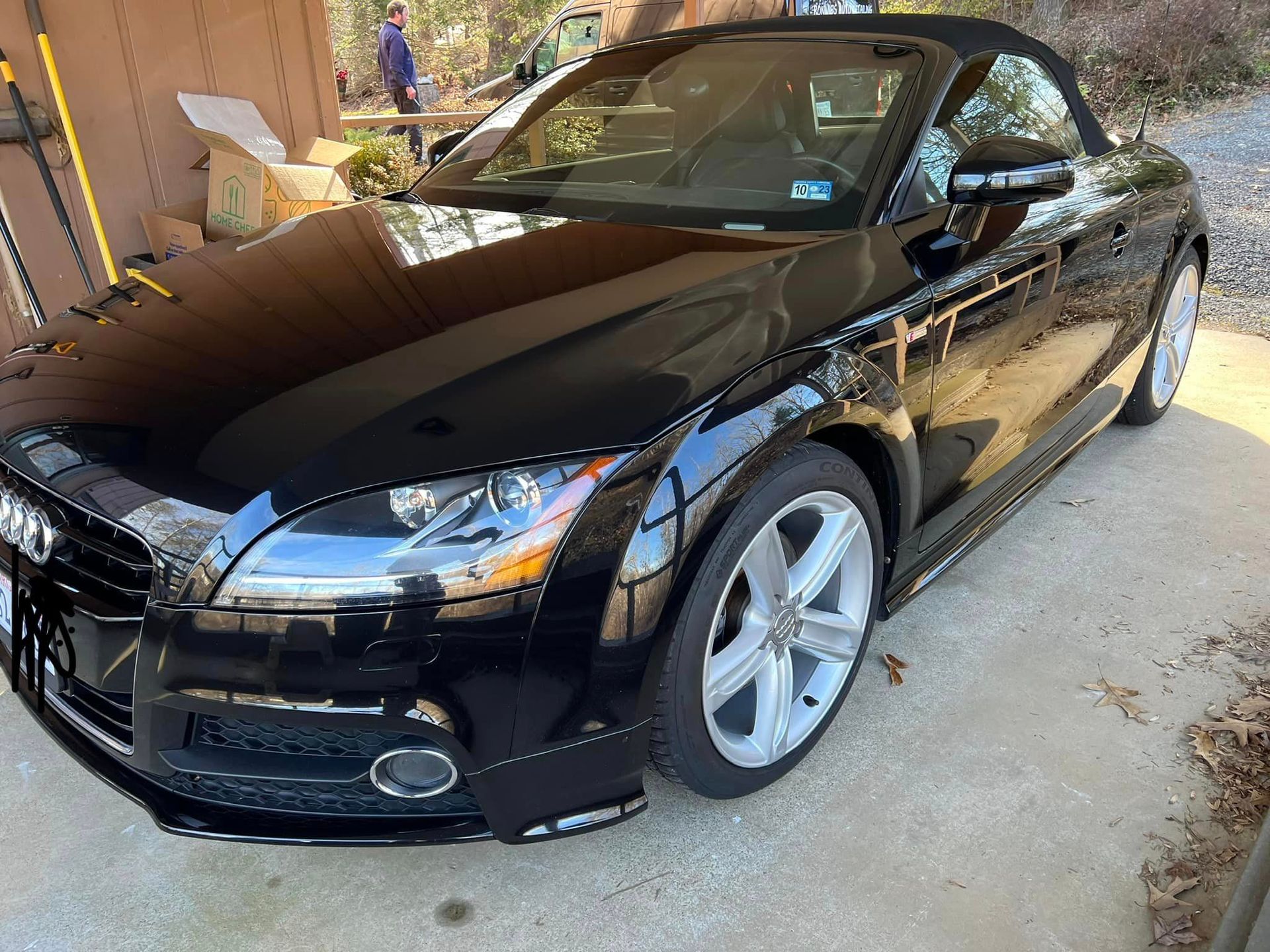 Black sports coupe parked in a driveway, front-left view under a covered carport.