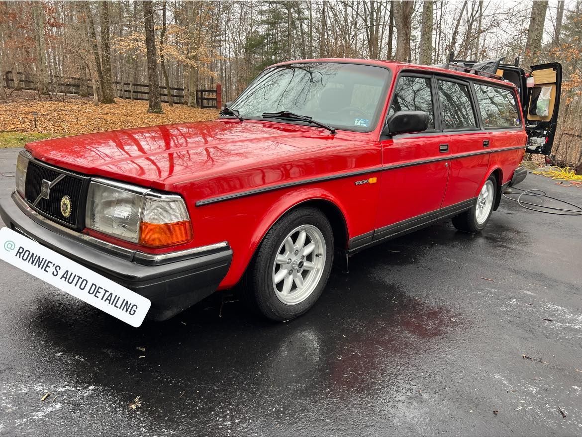Red vintage station wagon parked on a wet road beside bare trees, rear door open.