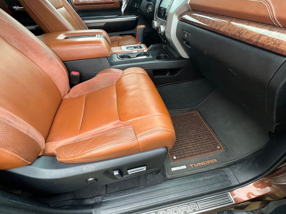 Tan leather SUV rear seat and center console with wood trim and black floor mat.