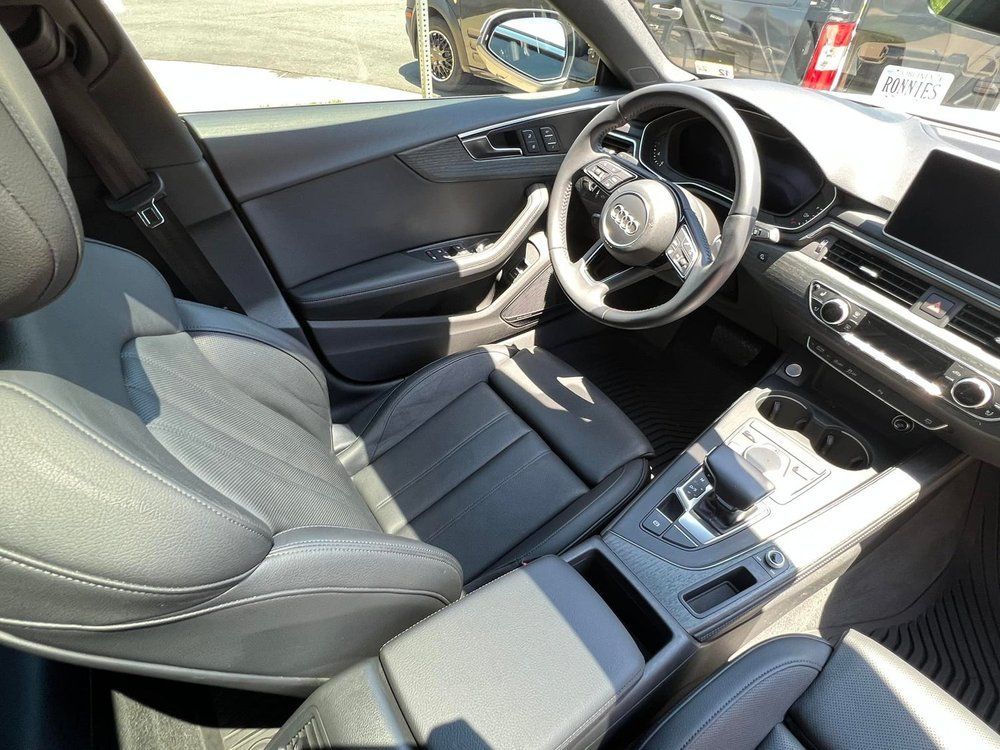 Car interior with gray seats, steering wheel, center console, and dashboard in sunlight.
