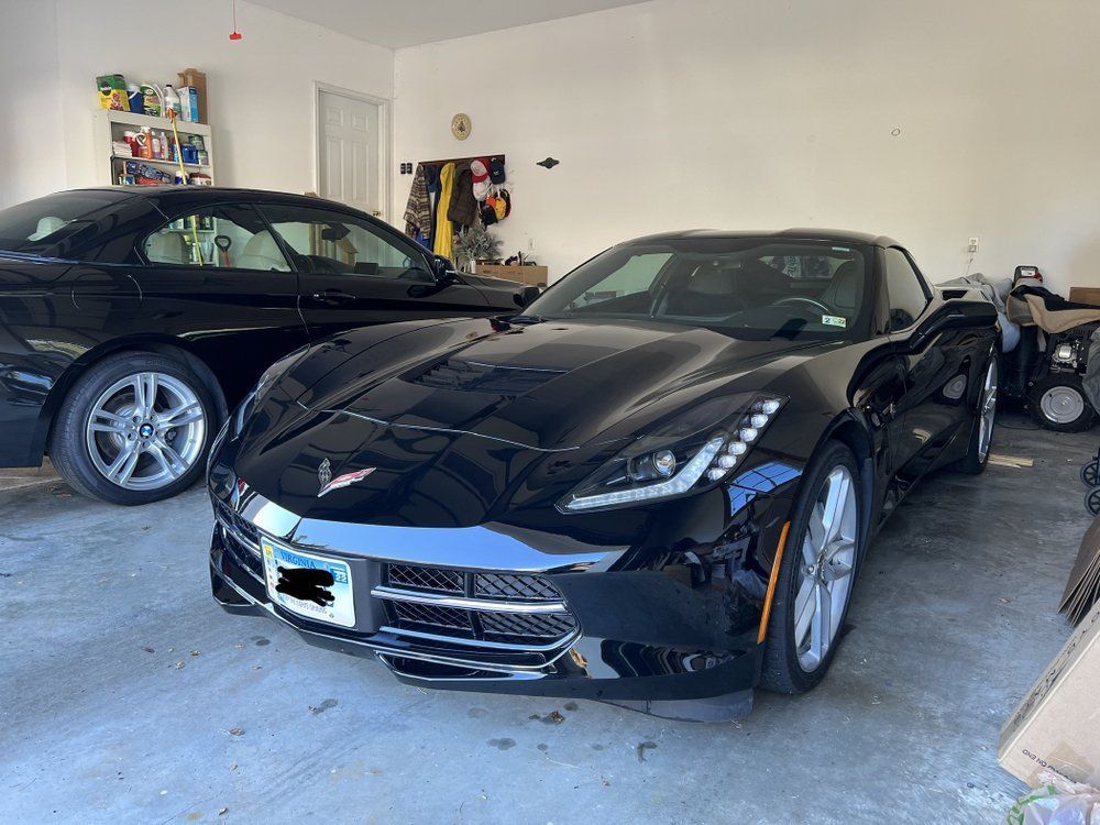 Two black cars parked in a garage, including a black sports car in front.