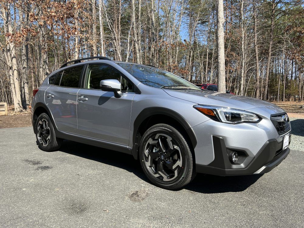 Silver Subaru crossover parked on pavement beside leafless trees under a clear sky