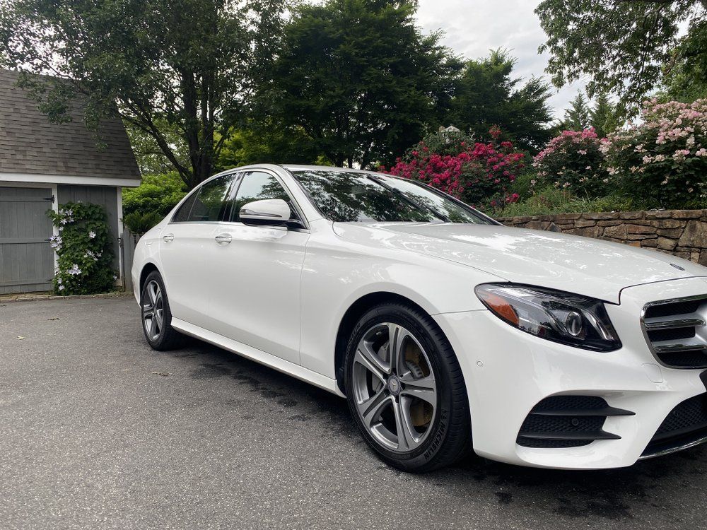 White Mercedes sedan parked in a driveway beside a stone wall and flowering bushes