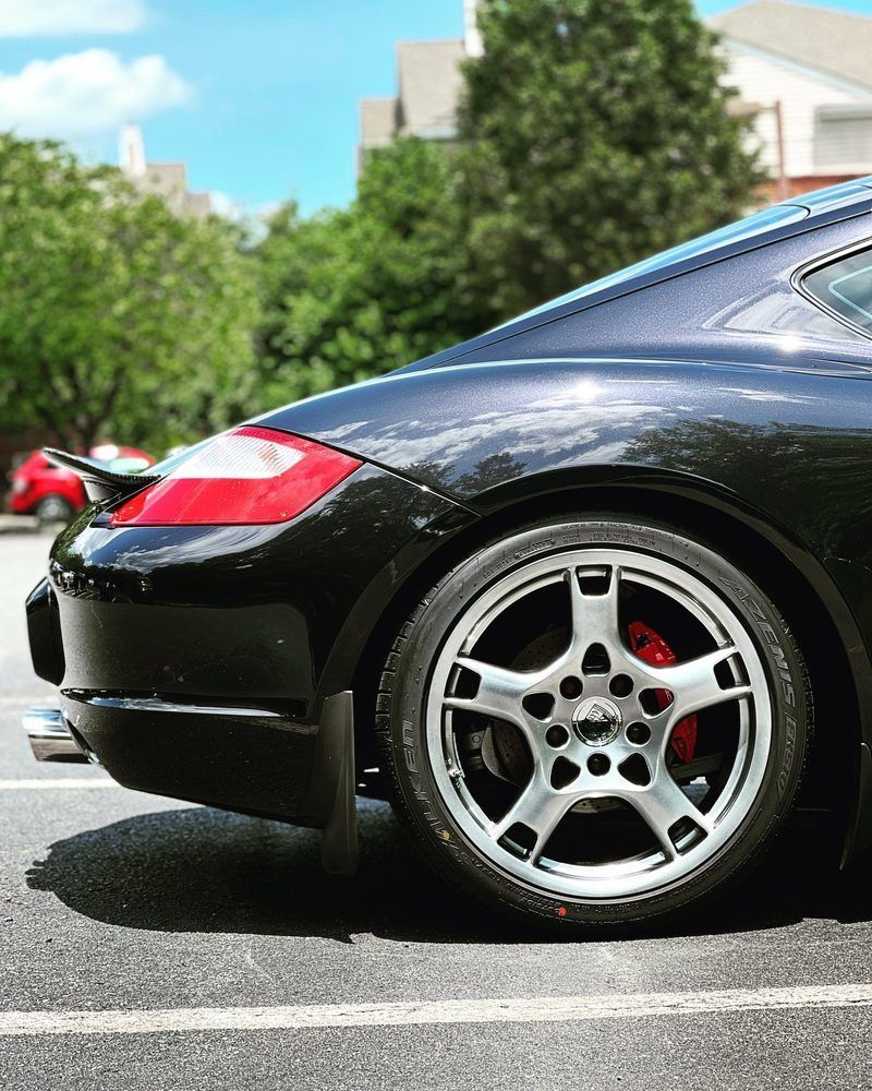 Black sports car rear side with silver wheel parked on a street, trees and houses in background