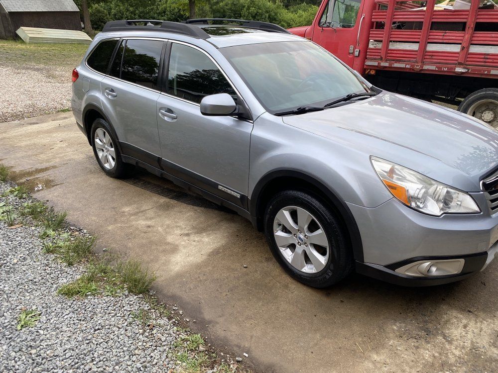 Silver SUV parked in a driveway beside a red truck and gravel driveway.