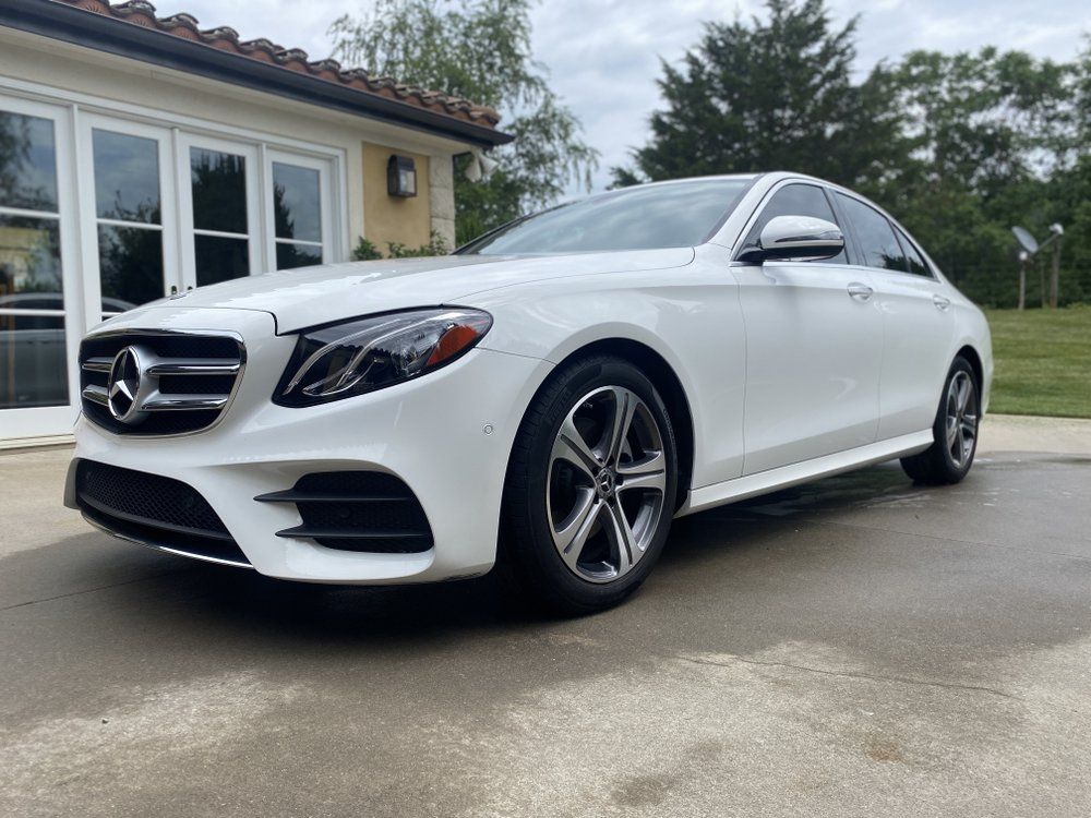 White Mercedes-Benz sedan parked on a driveway beside a house on a cloudy day