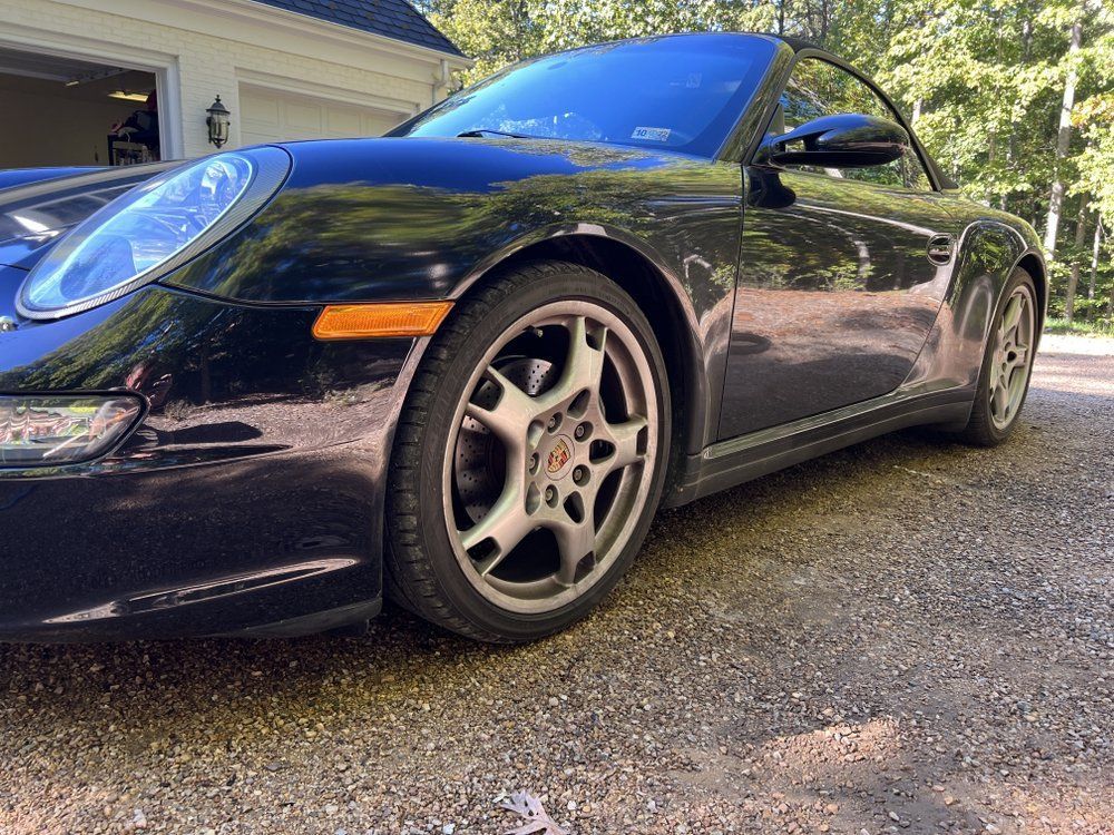 Black Porsche 911 parked in a driveway, low-angle view with a blue sky reflection on the hood