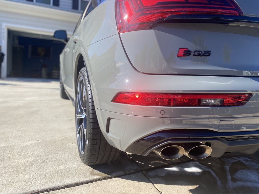 Rear view of a silver SUV with red taillights and dual exhaust pipes in a driveway