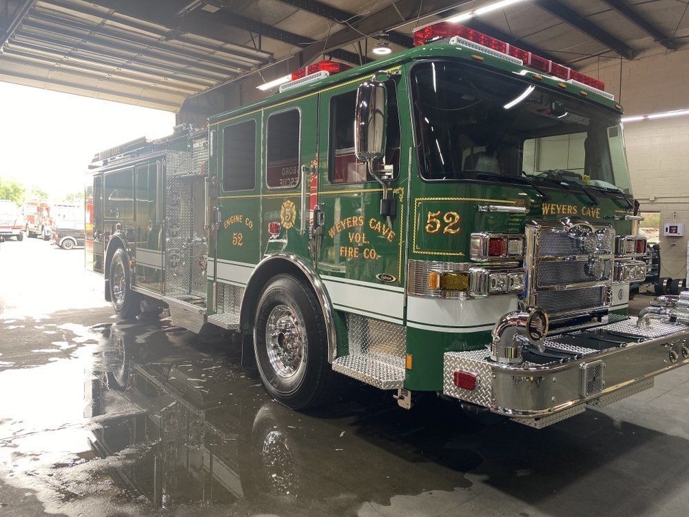 Green fire truck numbered 52 parked in a station bay, wet floor reflecting its chrome details