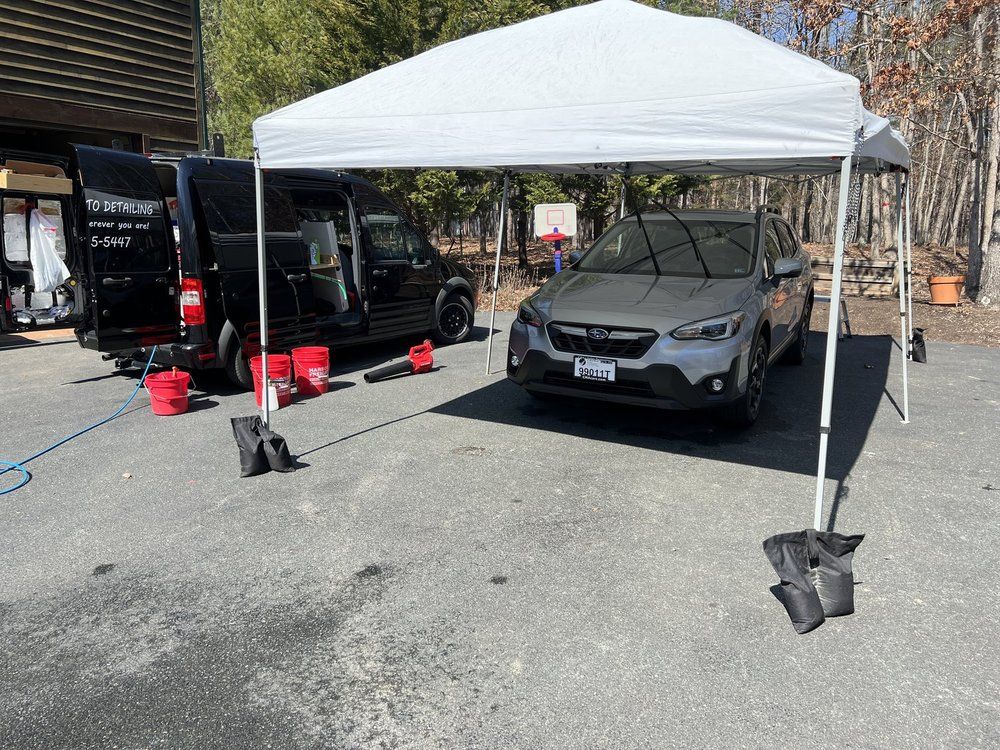 White canopy tent shading two parked cars at an outdoor auto detail setup, with buckets and supplies nearby