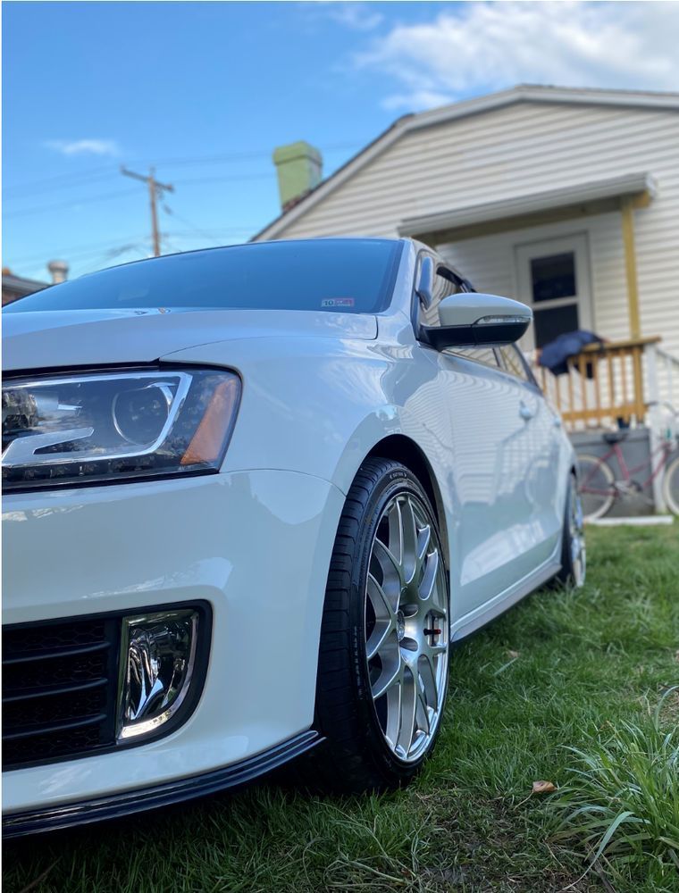White sedan with chrome wheels parked on grass beside a house on a sunny day