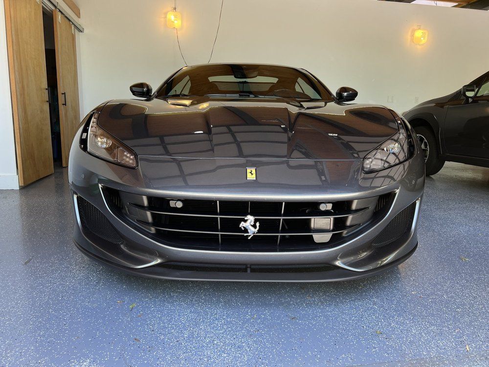 Dark gray Ferrari sports car parked in a garage, front view with a partially visible car beside it