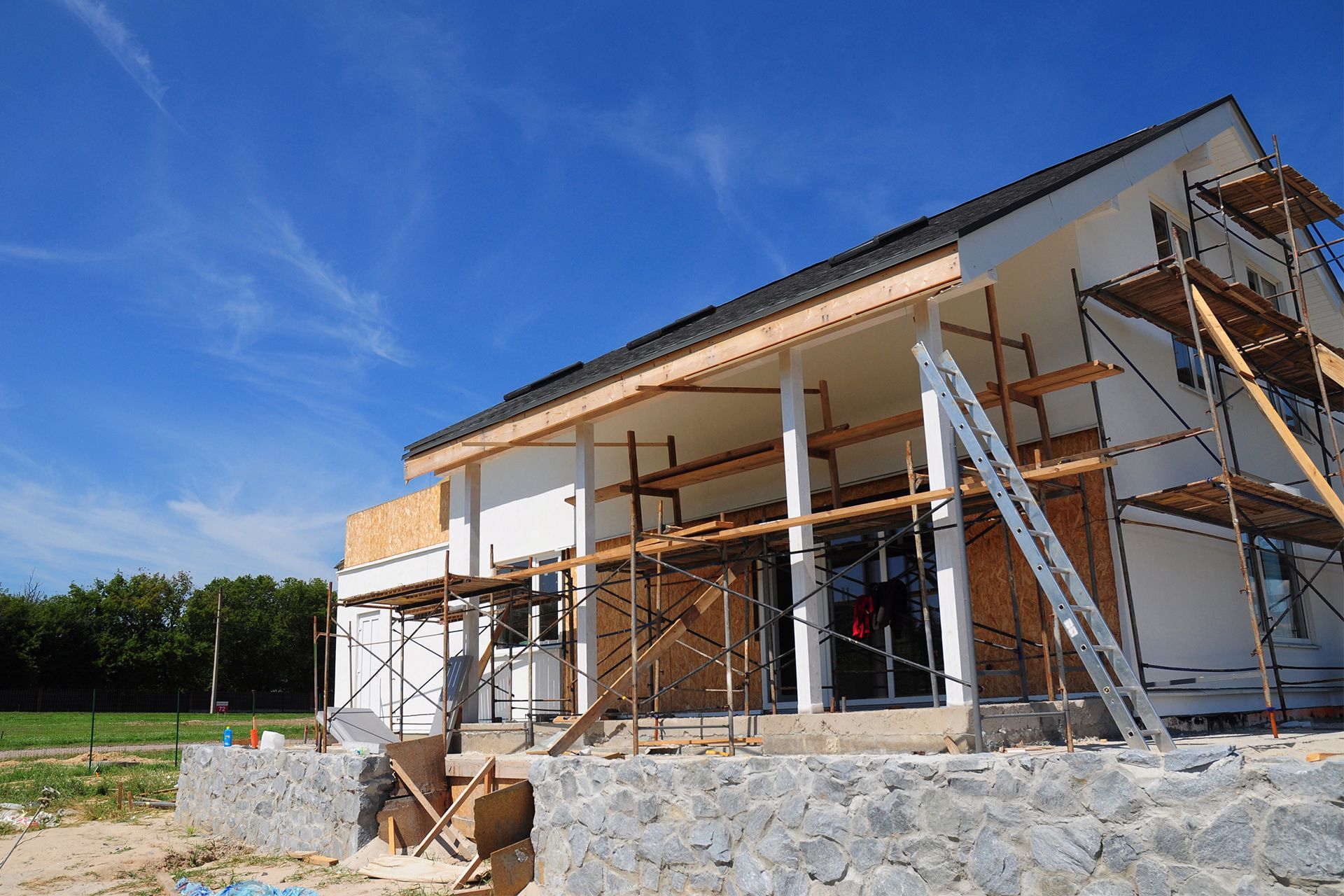 House under construction with white walls, scaffolding, and blue sky.