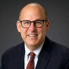 A bald man wearing glasses and a suit and tie is smiling for the camera.