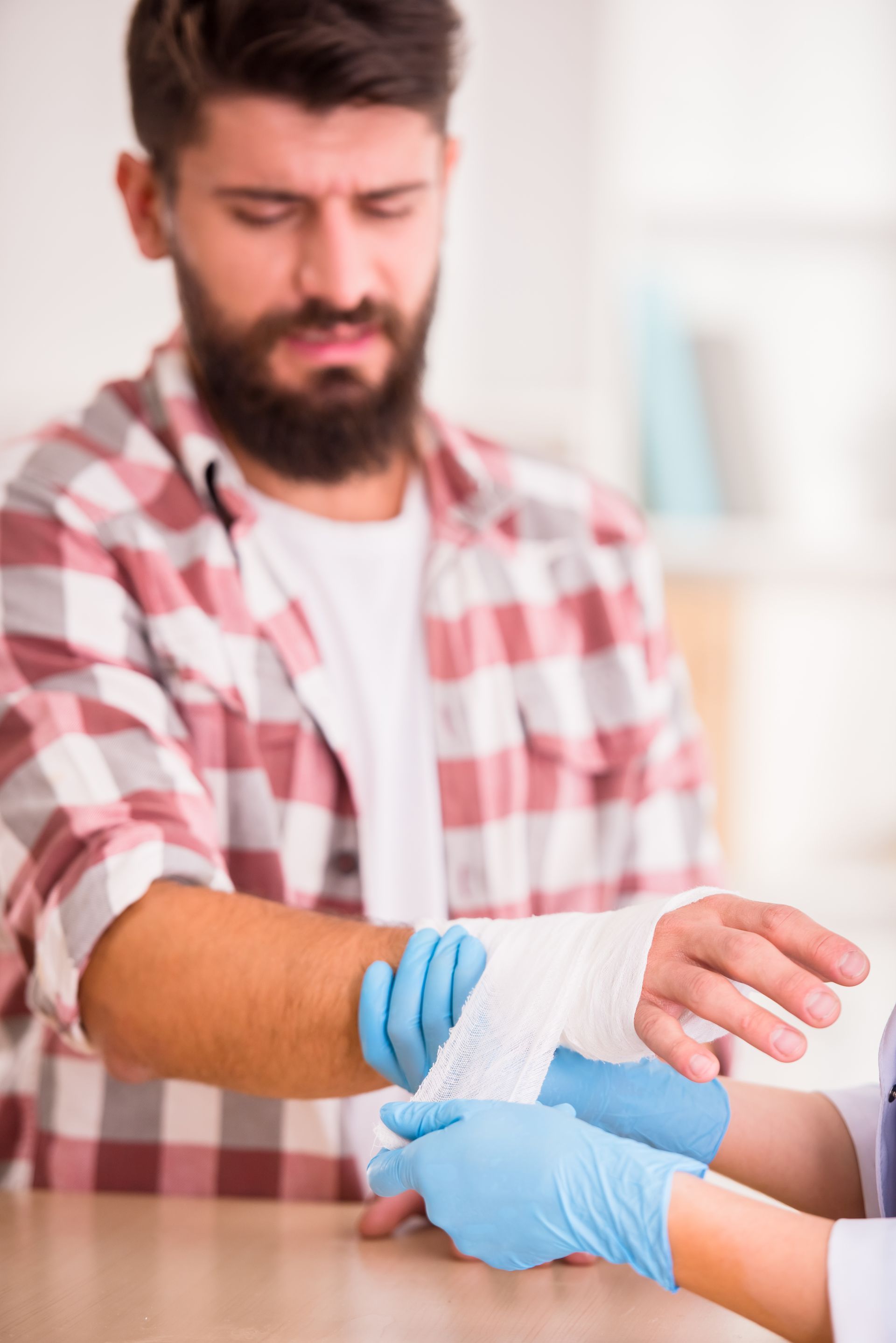 Person in plaid shirt with blue gloves wrapping a bandage around another person’s arm