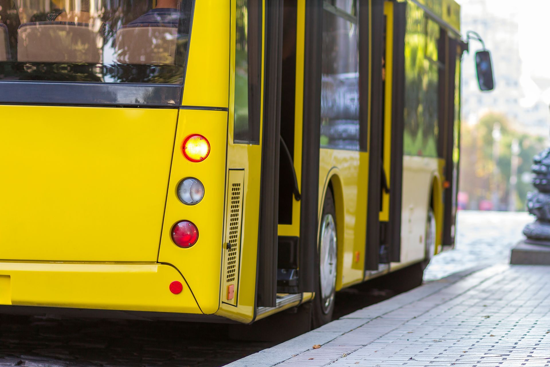 Yellow city bus parked by a sidewalk, rear view with doors open and tail lights visible