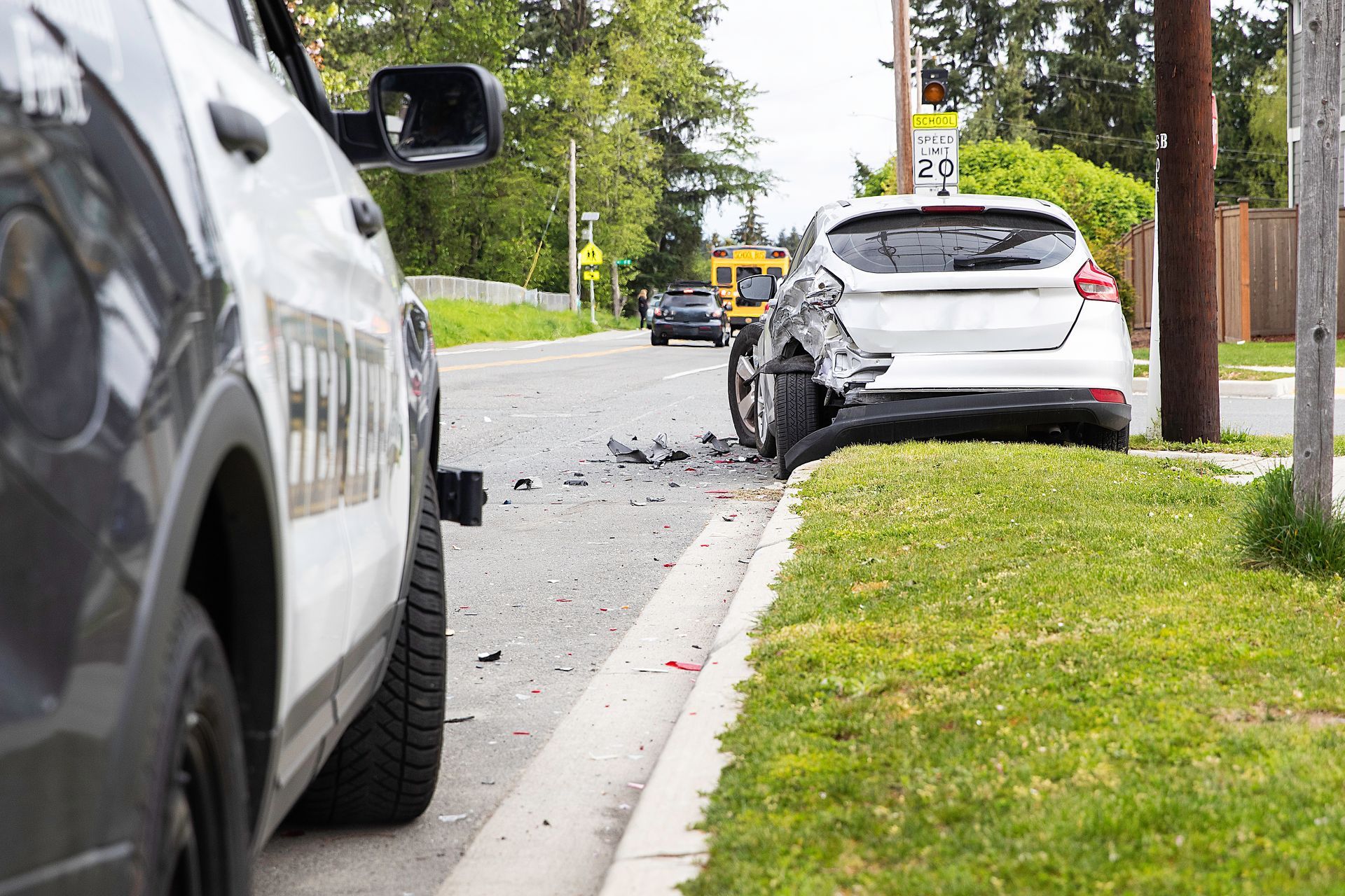 White SUV stopped on roadside after minor crash, with debris on the street and a police vehicle nearby.