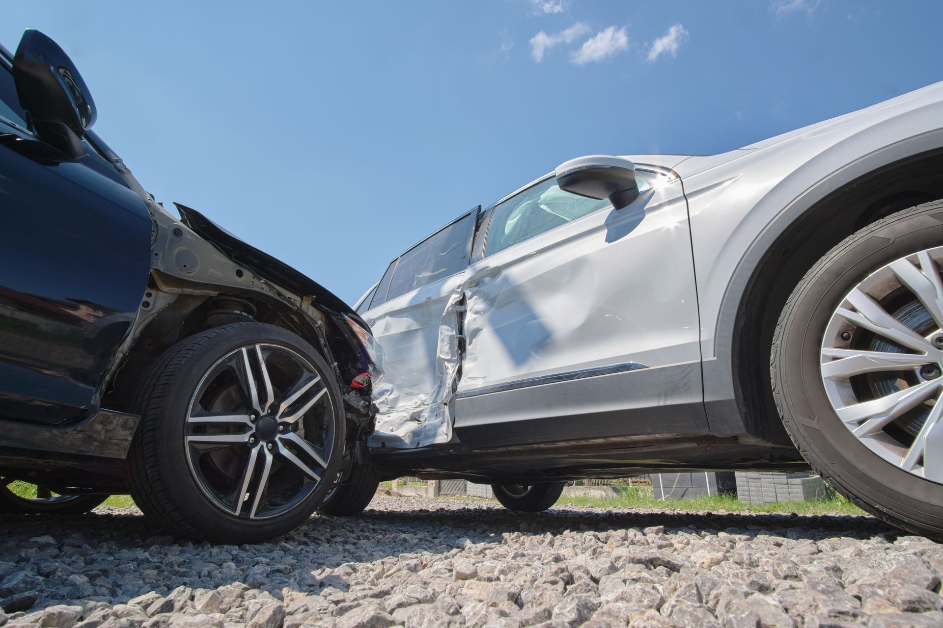 Two cars collided on a gravel road, with damage visible on the silver car's side.