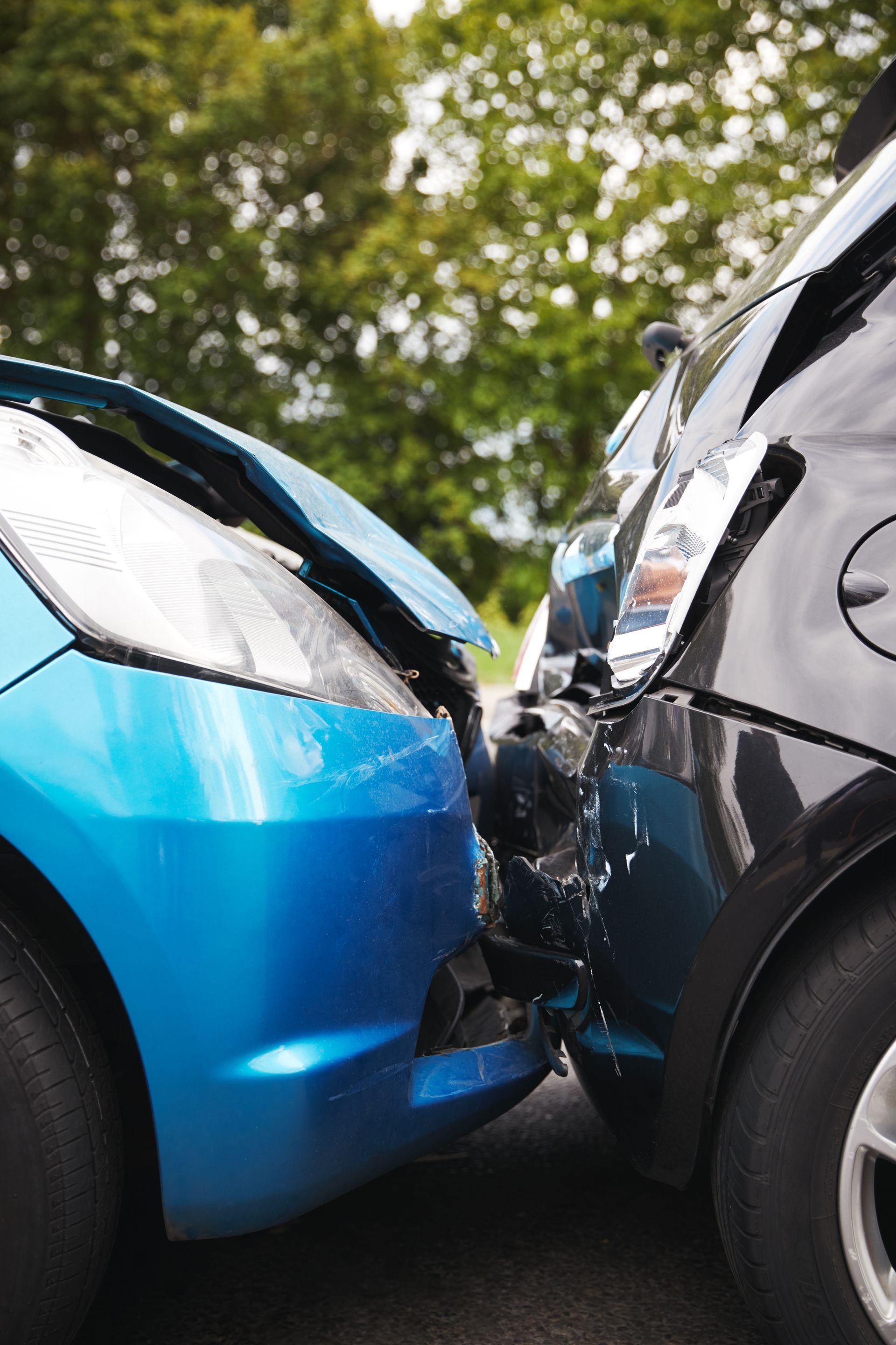 Blue car and black car with front-end collision on a road under trees