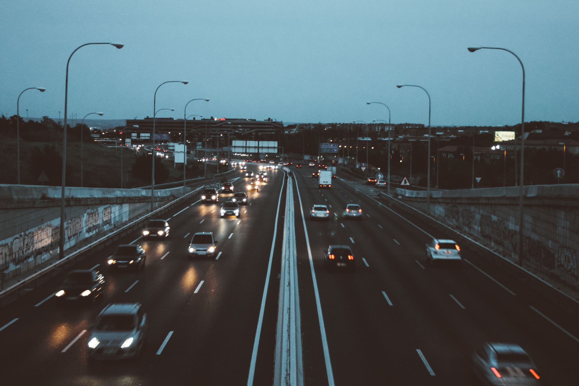Dusk highway scene with cars driving on wet lanes under blue sky and streetlights