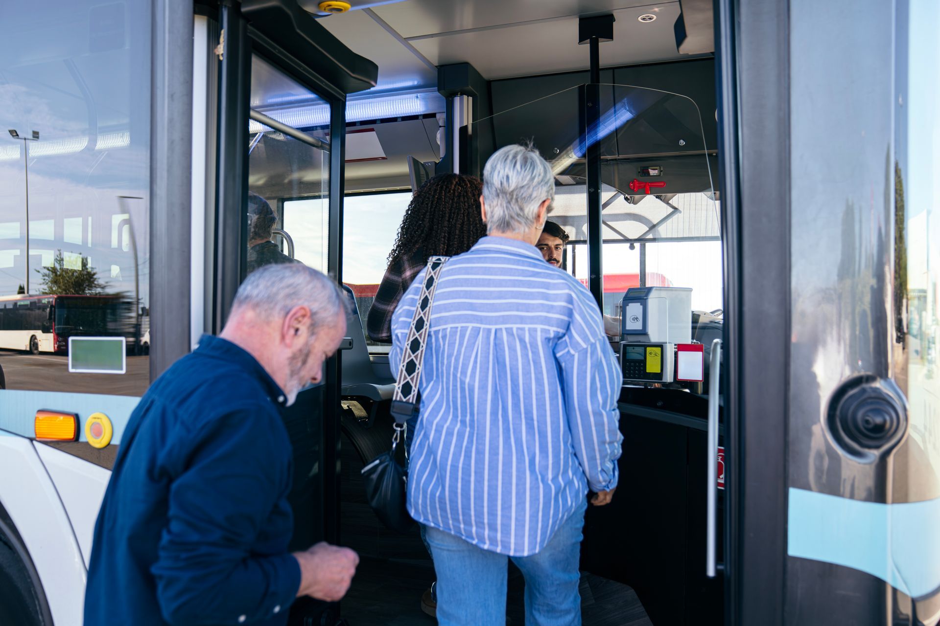 Two people boarding a city bus through the front door, one using the steps and handrails.