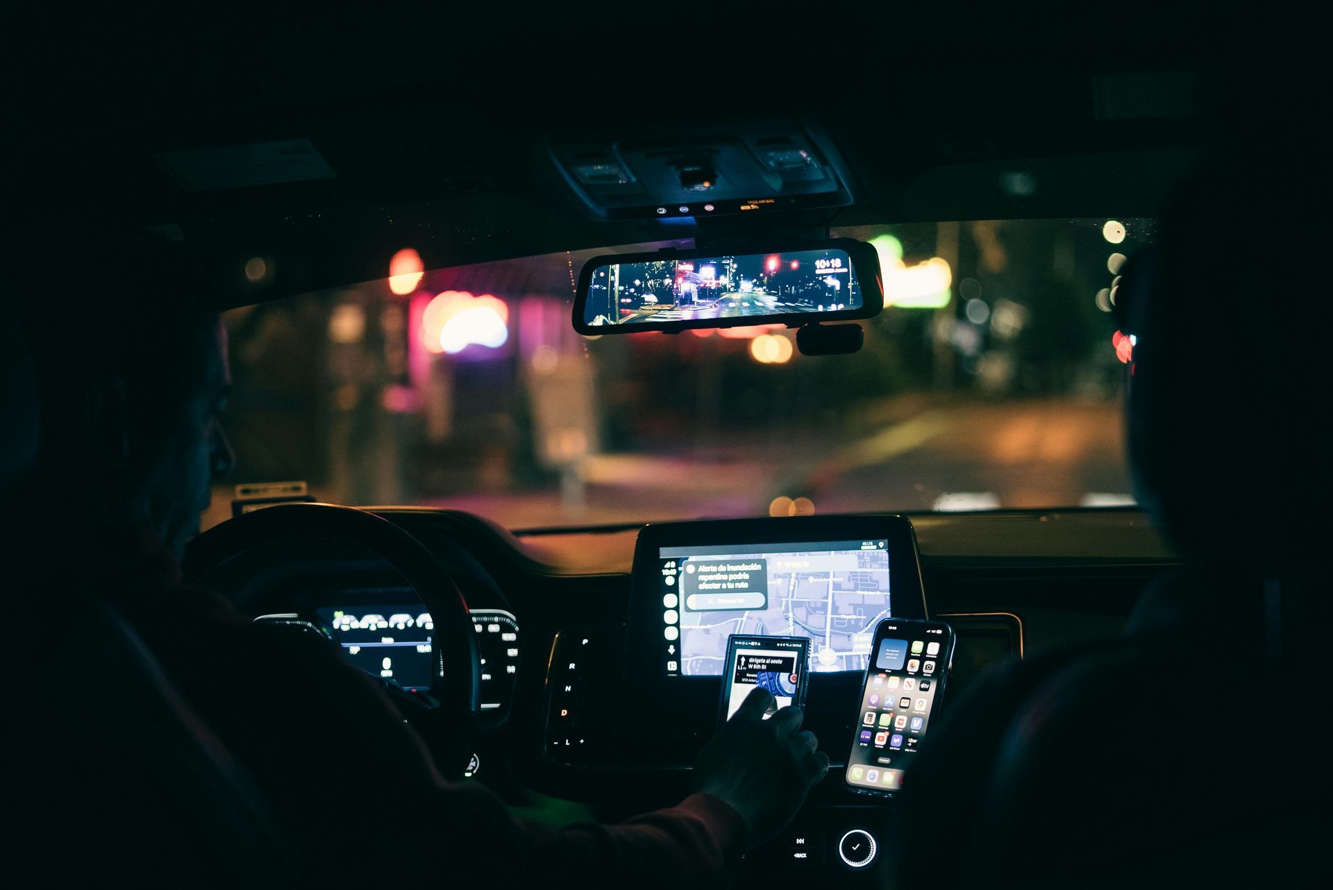 A person driving a car at night, with multiple glowing screens and a digital dashboard visible in the dark interior.