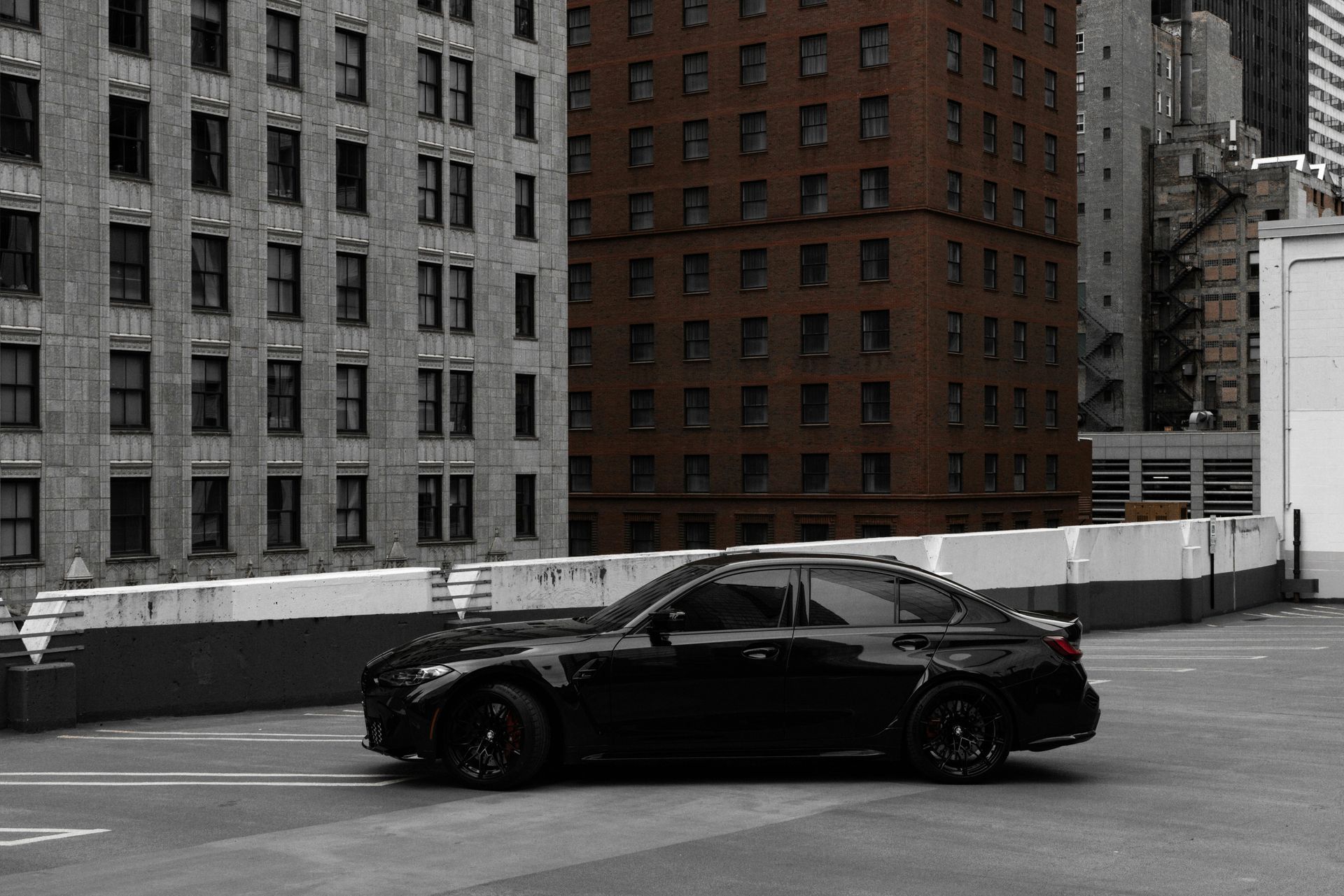 A black car is parked in a parking lot in front of a building.