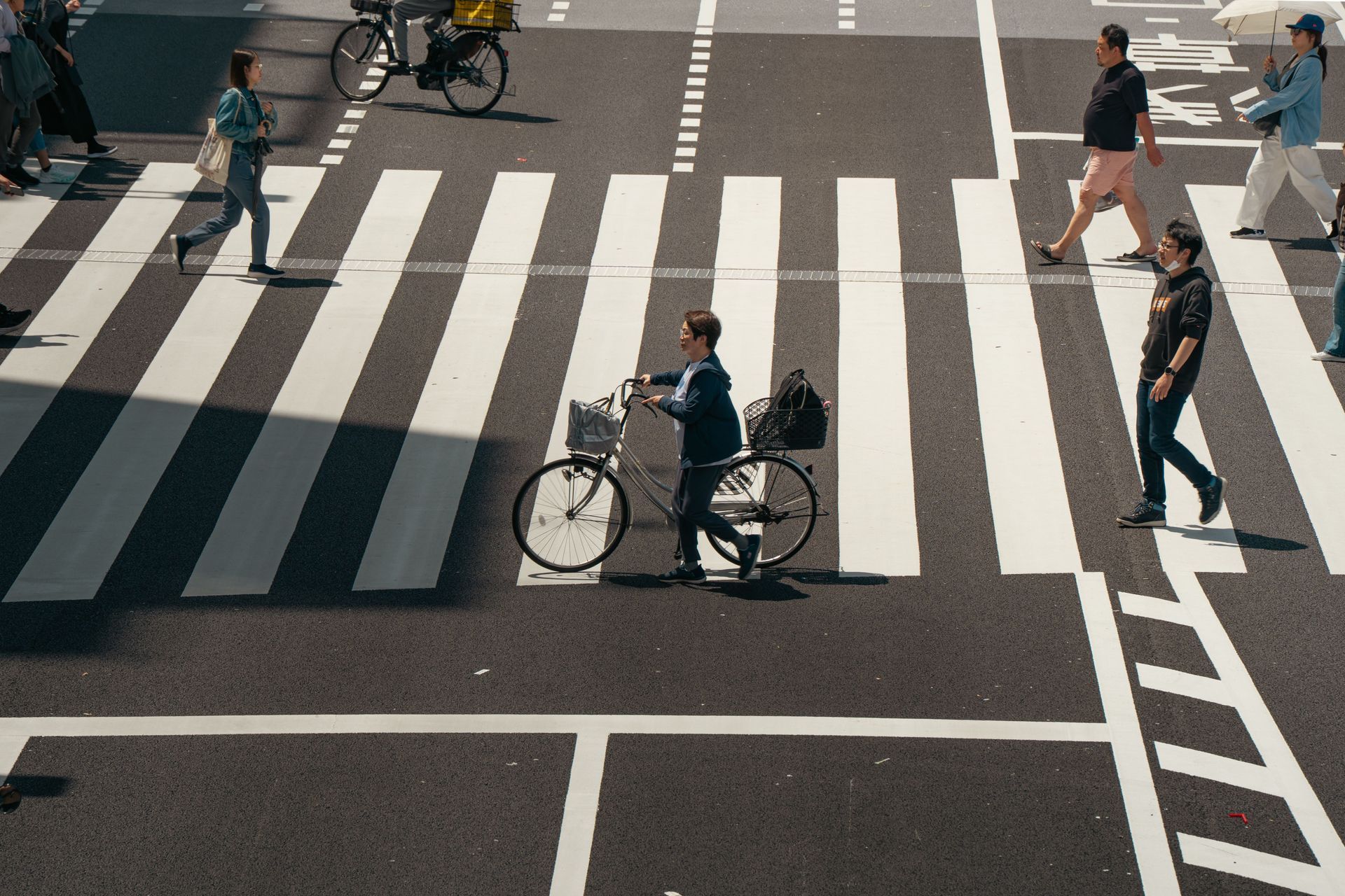 Cyclists and pedestrians crossing a city street at a marked crosswalk with bold white stripes