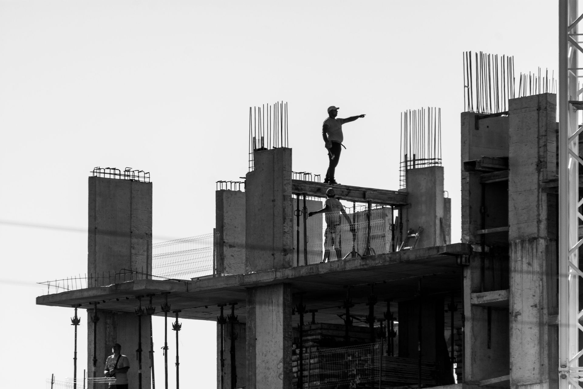 Construction worker standing on a high-rise scaffold, silhouetted against a gray sky