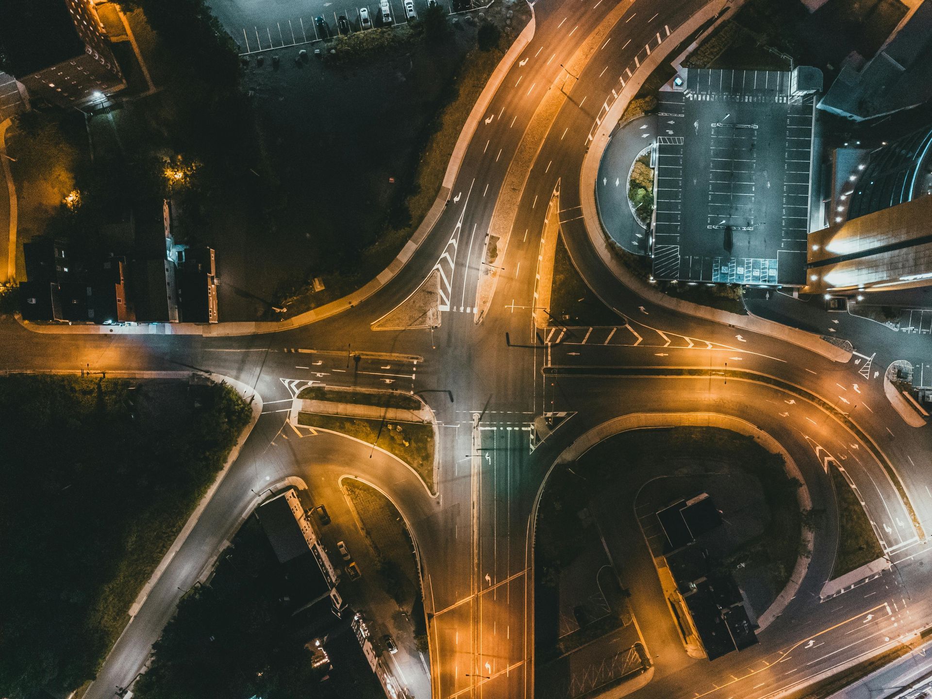 An overhead night view of a multi-lane road intersection illuminated by yellow streetlights, showing curved access ramps.
