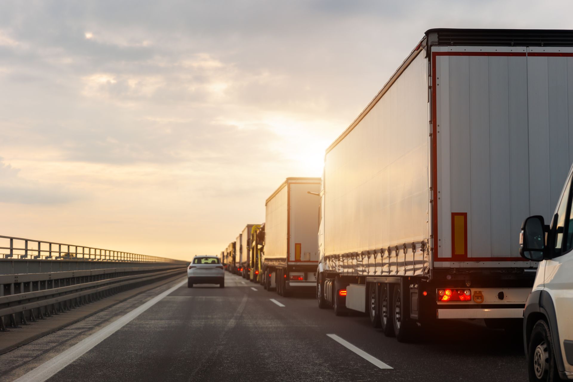 Trucks and cars driving on a highway at sunset with a bright sky