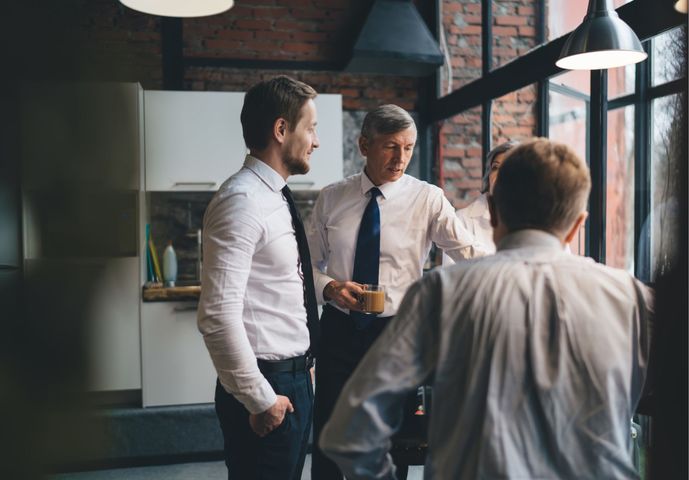 Three men talking in a modern office with large windows and hanging lights