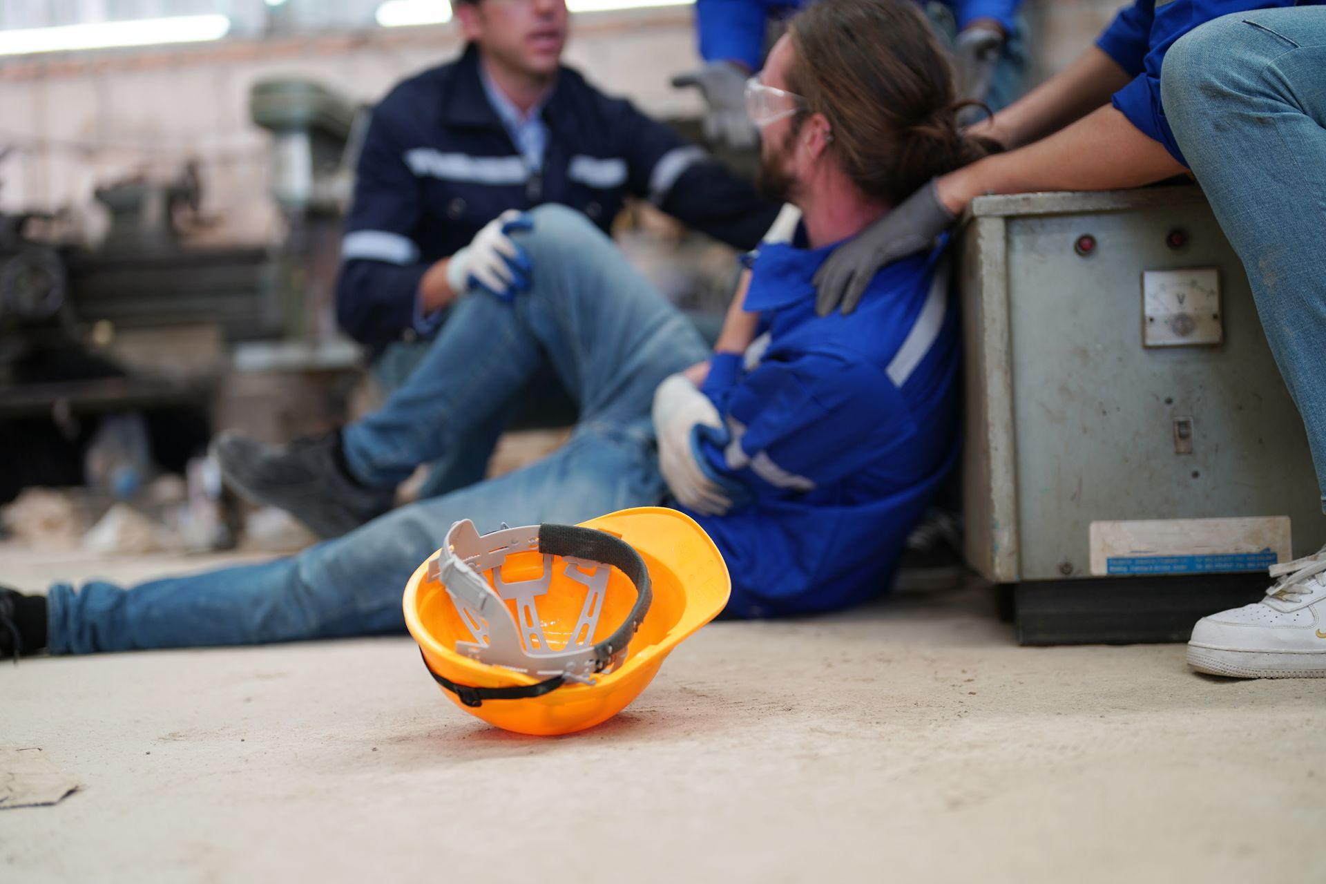 Orange hard hat with face shield on the ground beside two seated workers at a construction site.