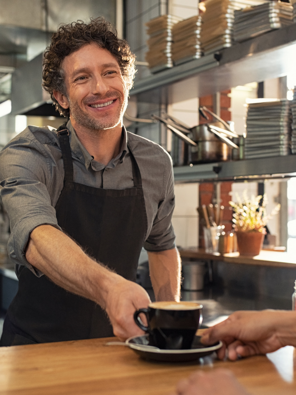 Un hombre con delantal sirve una taza de café a un cliente.