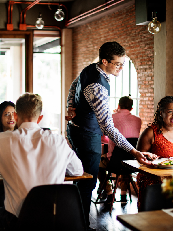 Un camarero sirve comida a un grupo de personas sentadas en las mesas de un restaurante.