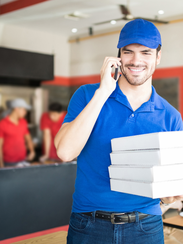 Un repartidor habla por teléfono celular mientras sostiene una pila de cajas de pizza.