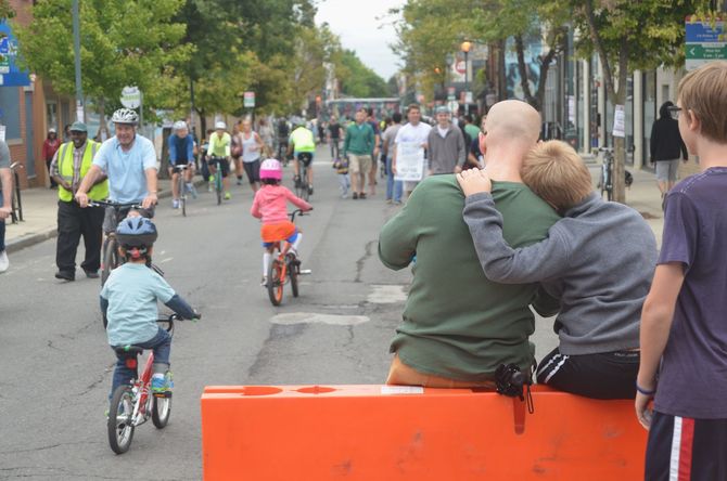 People ride bikes on a closed street. A man hugs a boy; other people walk and watch.