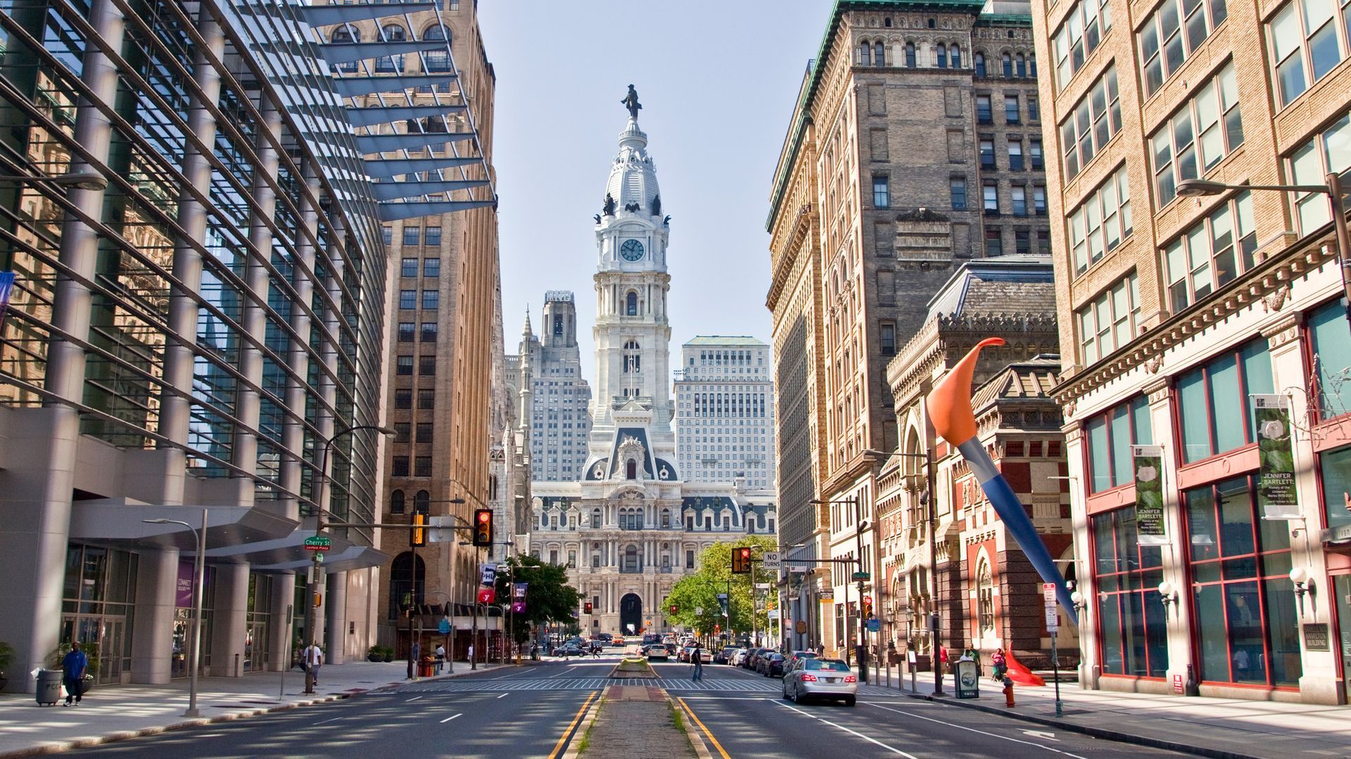 Philadelphia street view with City Hall in the distance, surrounded by tall buildings, sunny day.